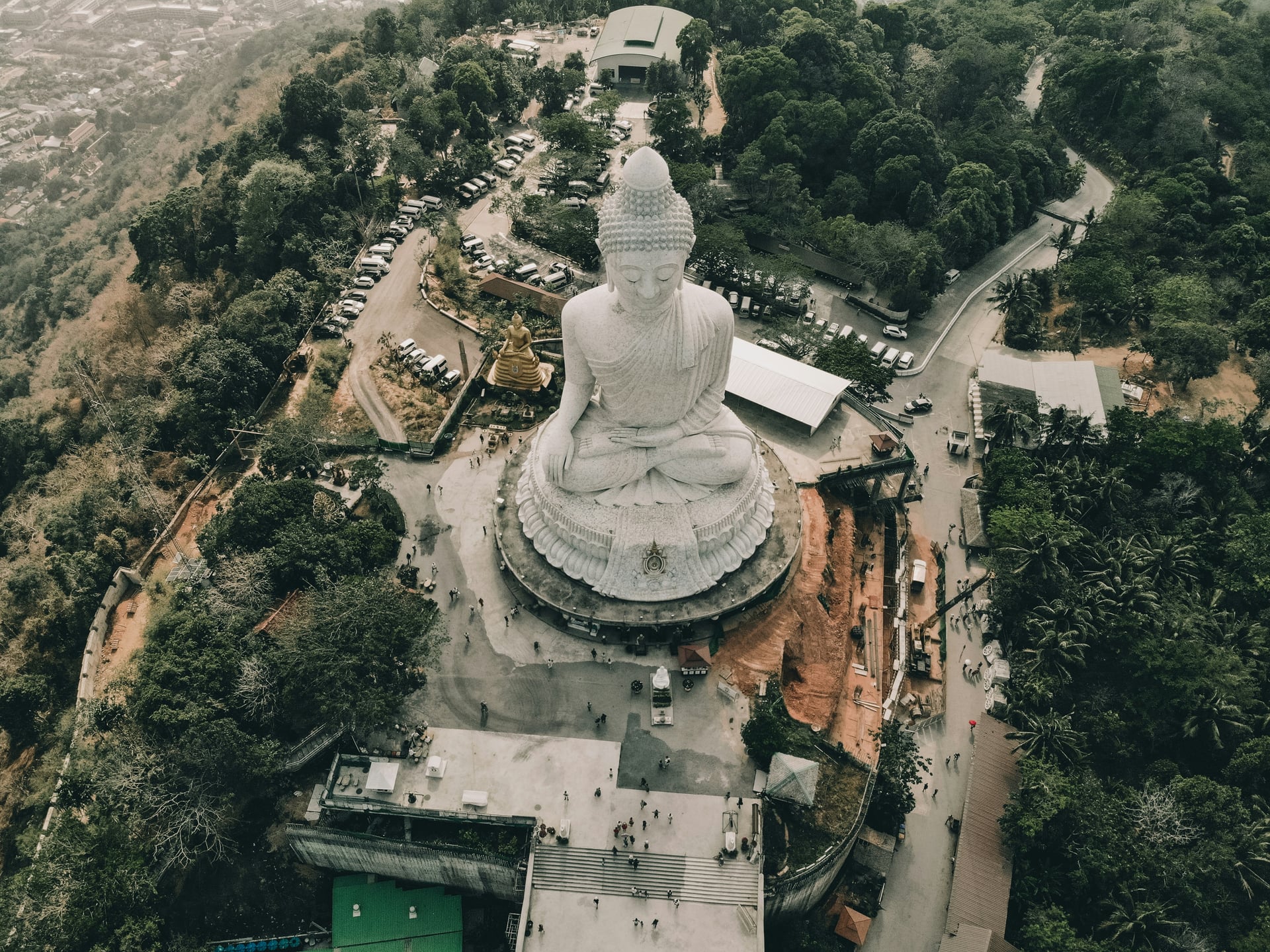 Aerial view of the Big Buddha statue surrounded by forest and hillside roads in Phuket, Thailand.