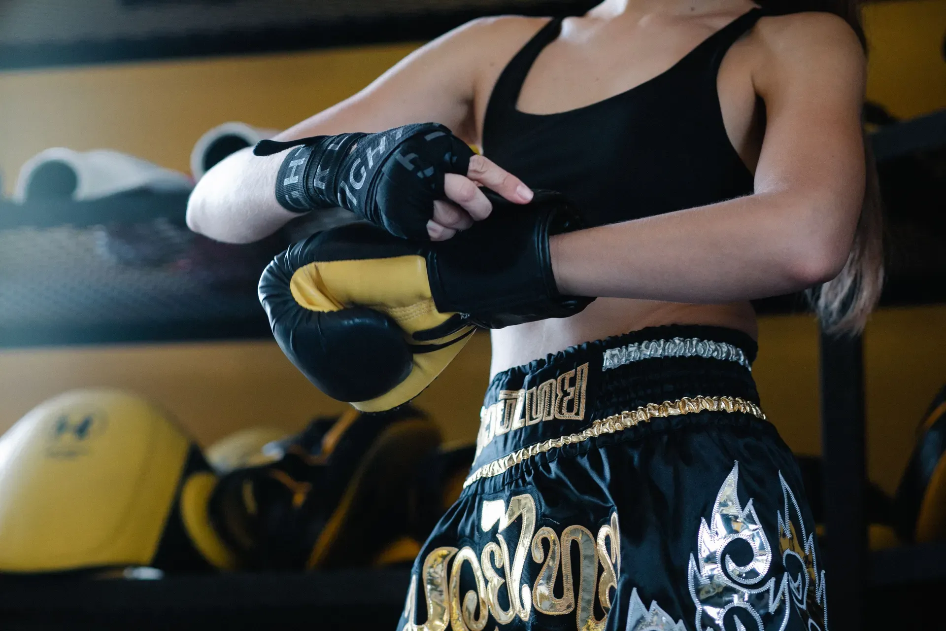A guest wrapping her hands and pulling on Muay Thai gloves in traditional Thai boxing shorts at the Phuket fit camp
