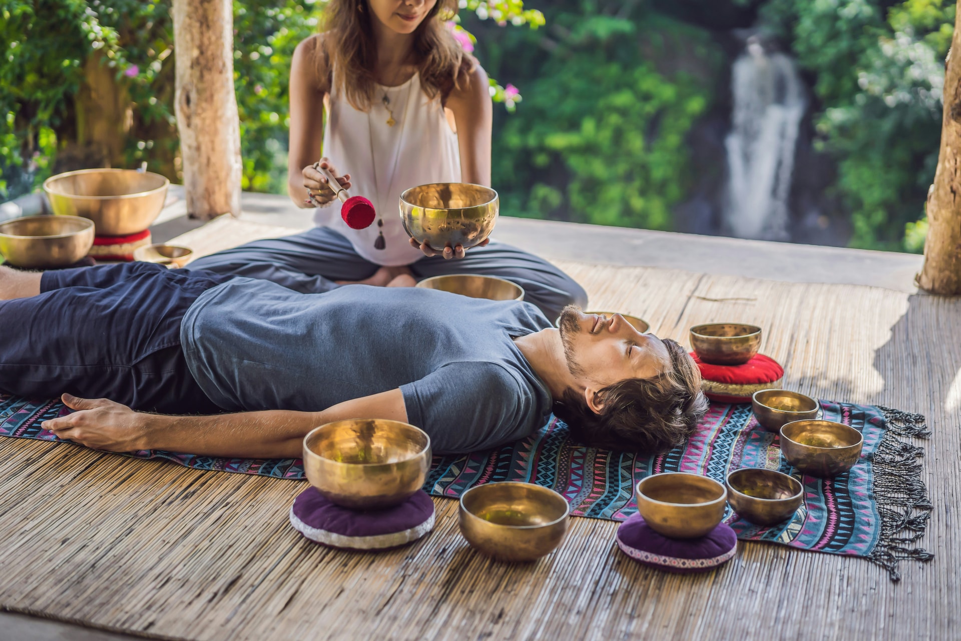 Wellness practitioner arranging Tibetan singing bowls and ritual objects for a sound healing session in Thailand