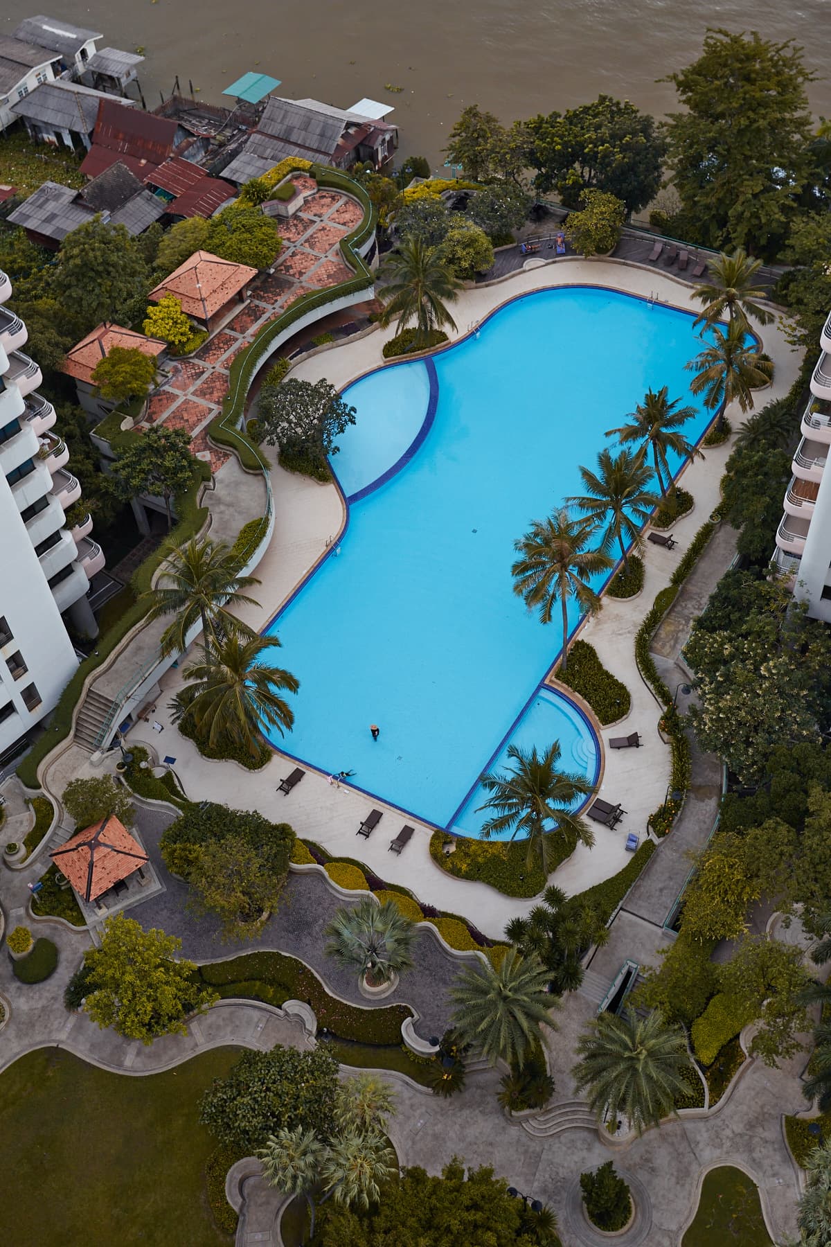Aerial view of Riverine Place Hotel with swimming pool and palm trees on the Chao Phraya River